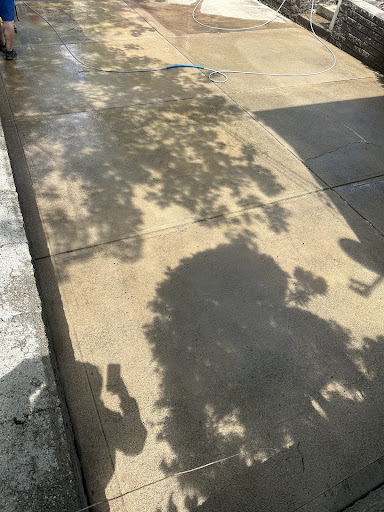 A driveway and sidewalk showing a sharp visible line between the untouched dirty concrete and the freshly pressure washed clean concrete